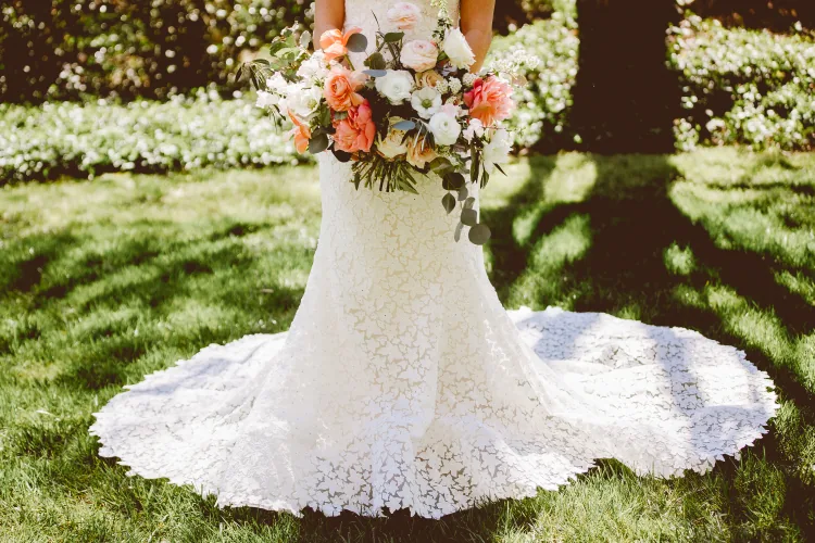 A lace gown and a bouquet of peach and white flowers on the grass