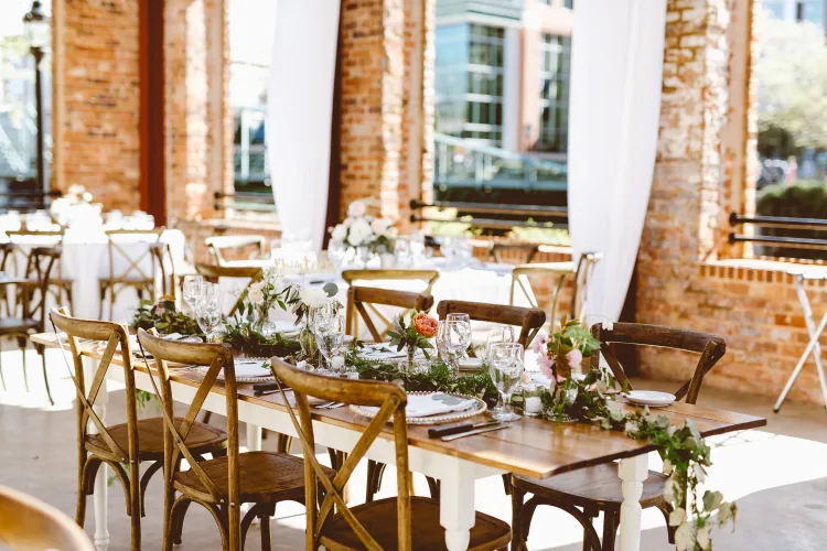 Long reception tables with greenery under brick arches, set before the guests arrive