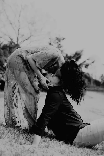 A woman leaning down to kiss her partner lying in the grass, in black and white