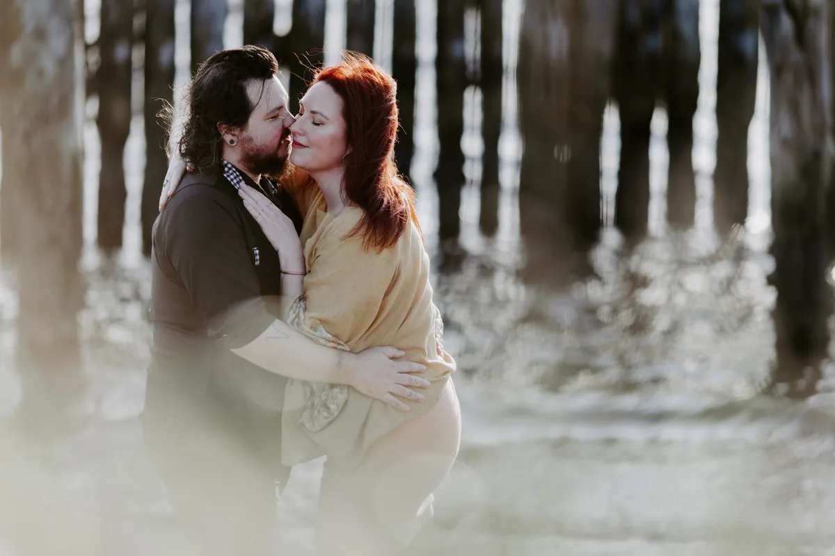 A couple kissing beneath a wooden pier